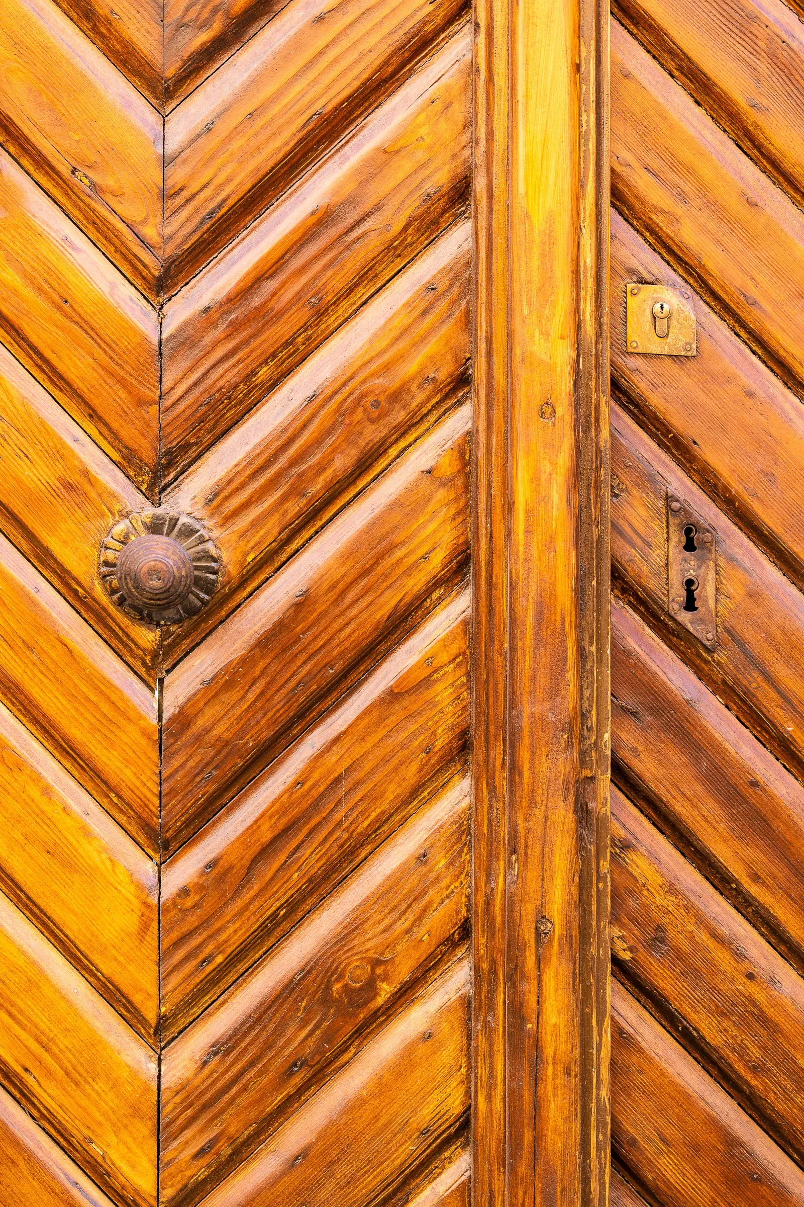 Close-up of a weathered wooden door with chevron-pattern panels and a brass keyhole plate.