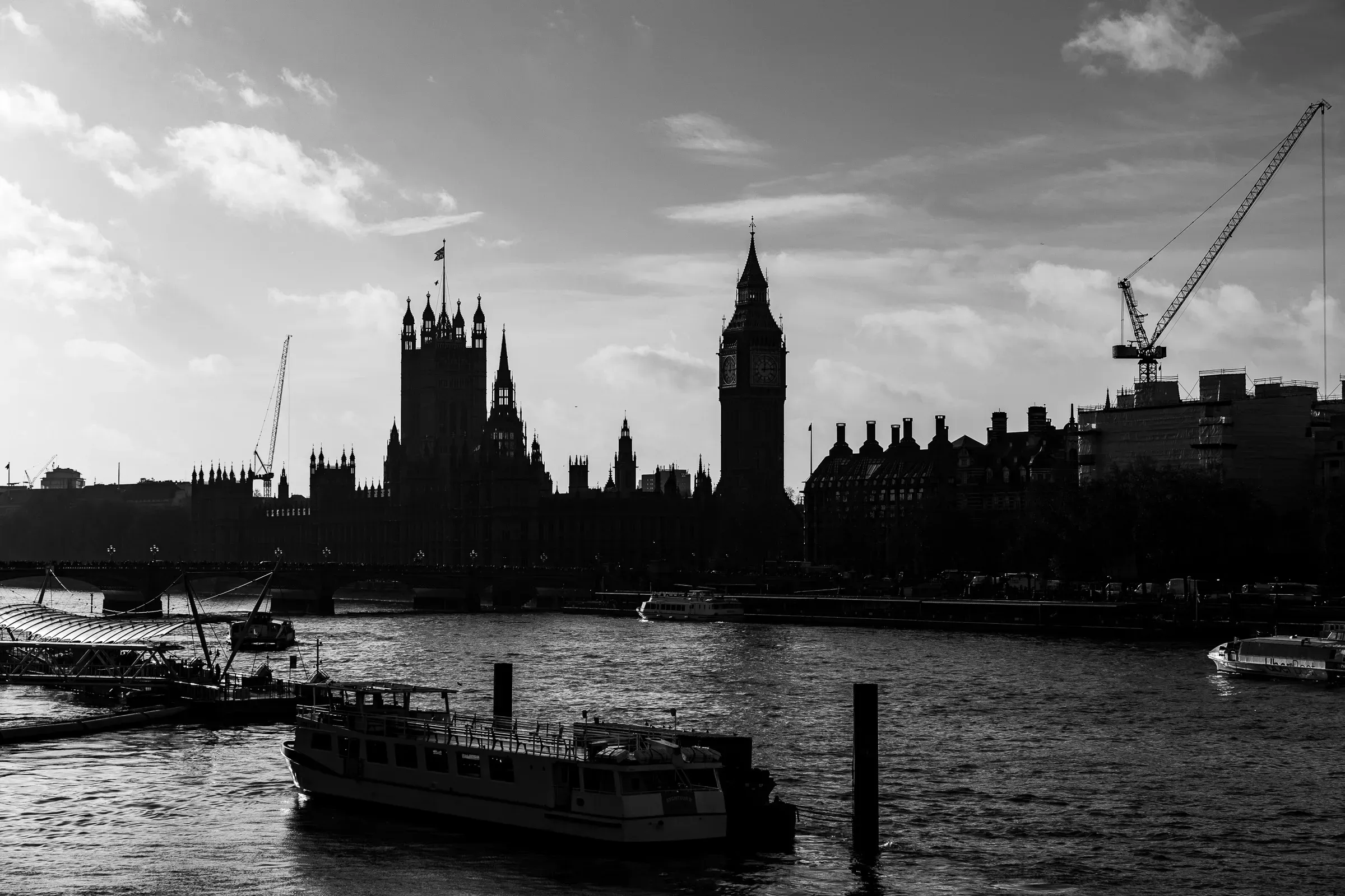 Silhouette of the Houses of Parliament and Elizabeth Tower at dusk, a tour boat on the Thames in the foreground, black and white
