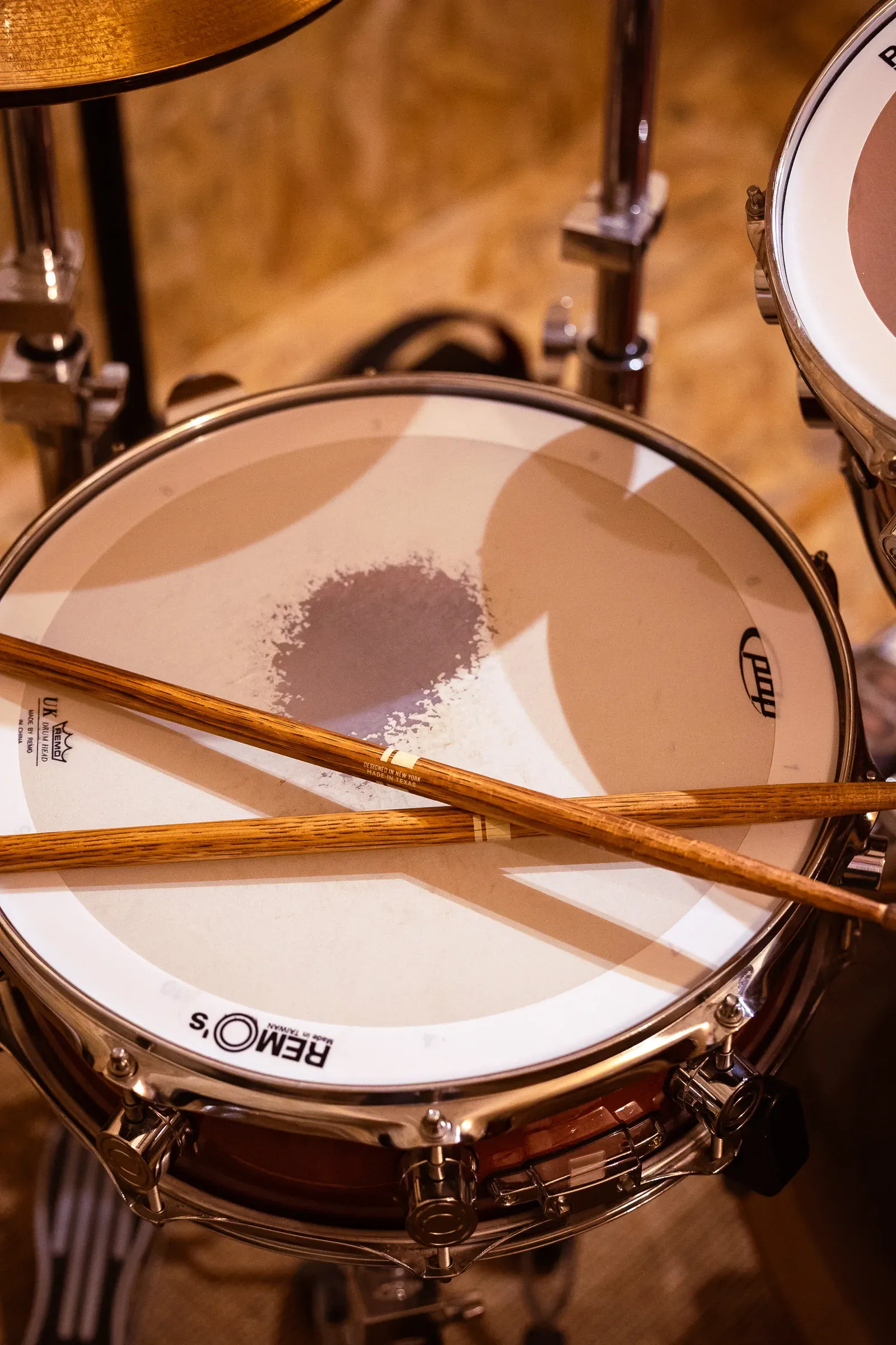 Top-down view of a Remo snare drum head with two wooden drumsticks crossed on top, Lyon