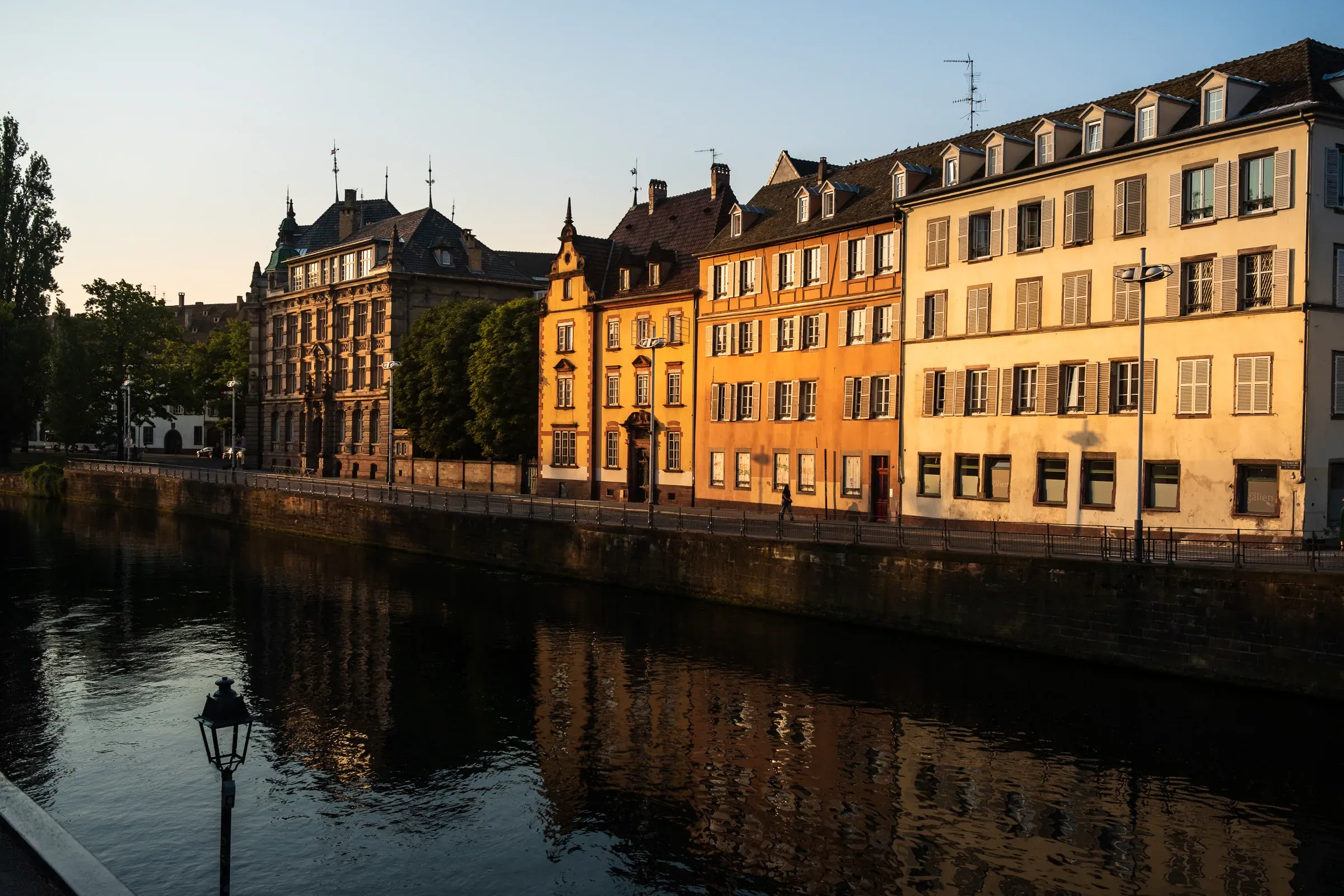 Canal-side buildings in Strasbourg lit orange by the evening sun, reflected in the water.