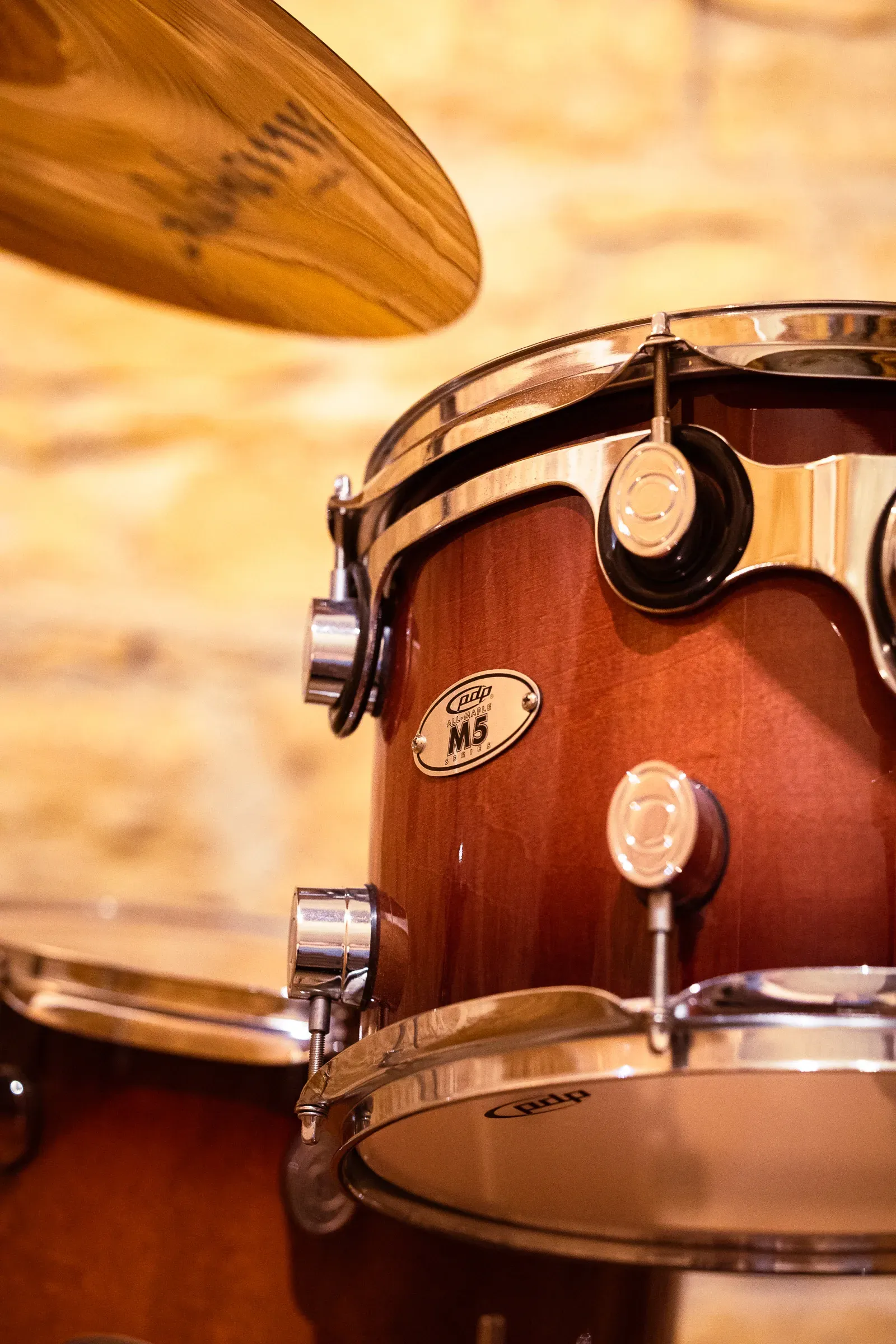 Close-up of a PDP M5 tom, chrome hardware catching the light, an Alchemy cymbal above, stone wall behind, Lyon