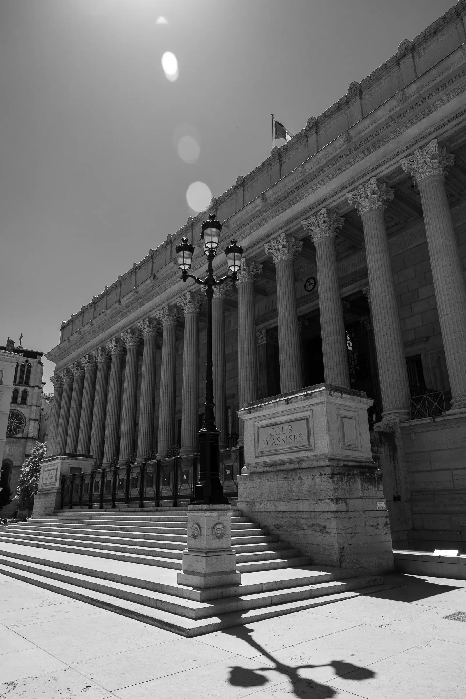 Black and white shot of the Palais de Justice neoclassical columns with a street lamp, Lyon