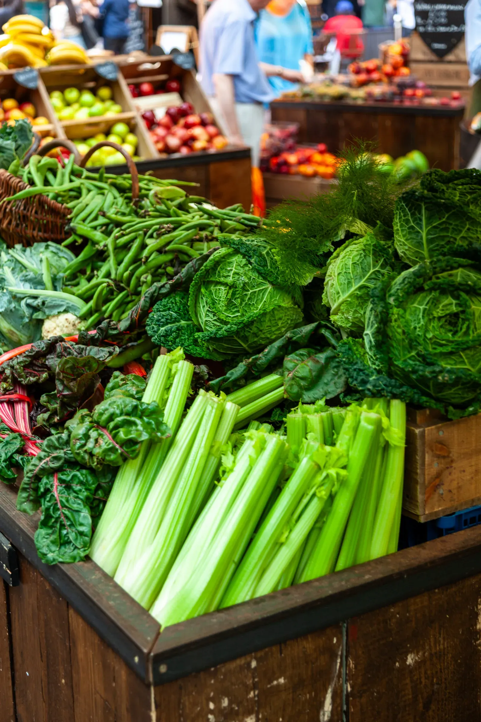 Overflowing wooden crates of green vegetables — celery, savoy cabbage, chard, runner beans, fennel — at a Borough Market stall