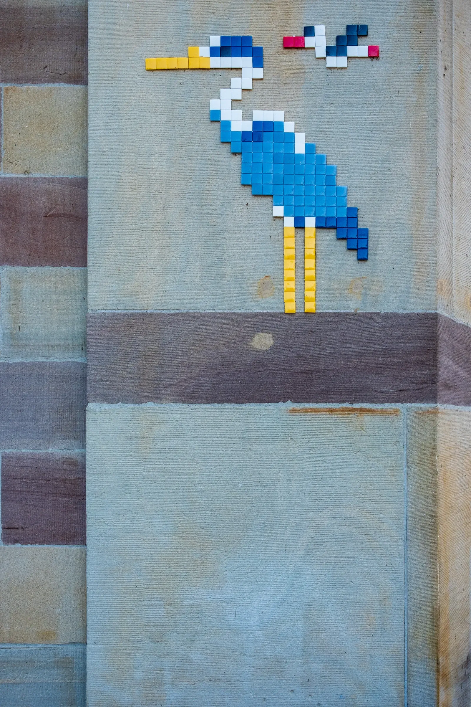 A pixel-mosaic street-art heron on a stone wall.