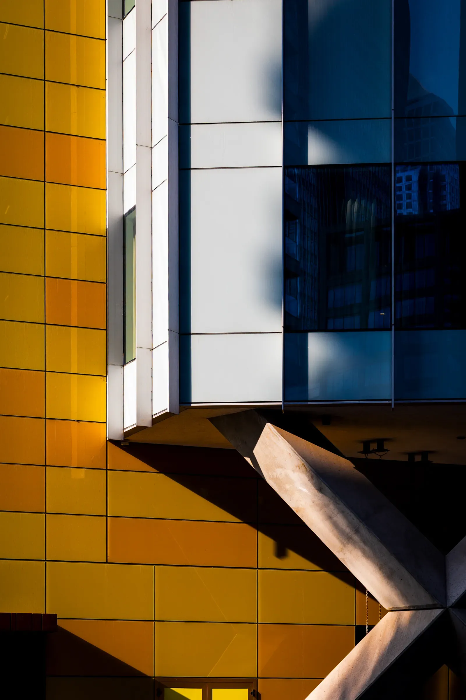 Abstract corner of a building in yellow, white and blue-glass panels, a concrete beam casting a diagonal shadow