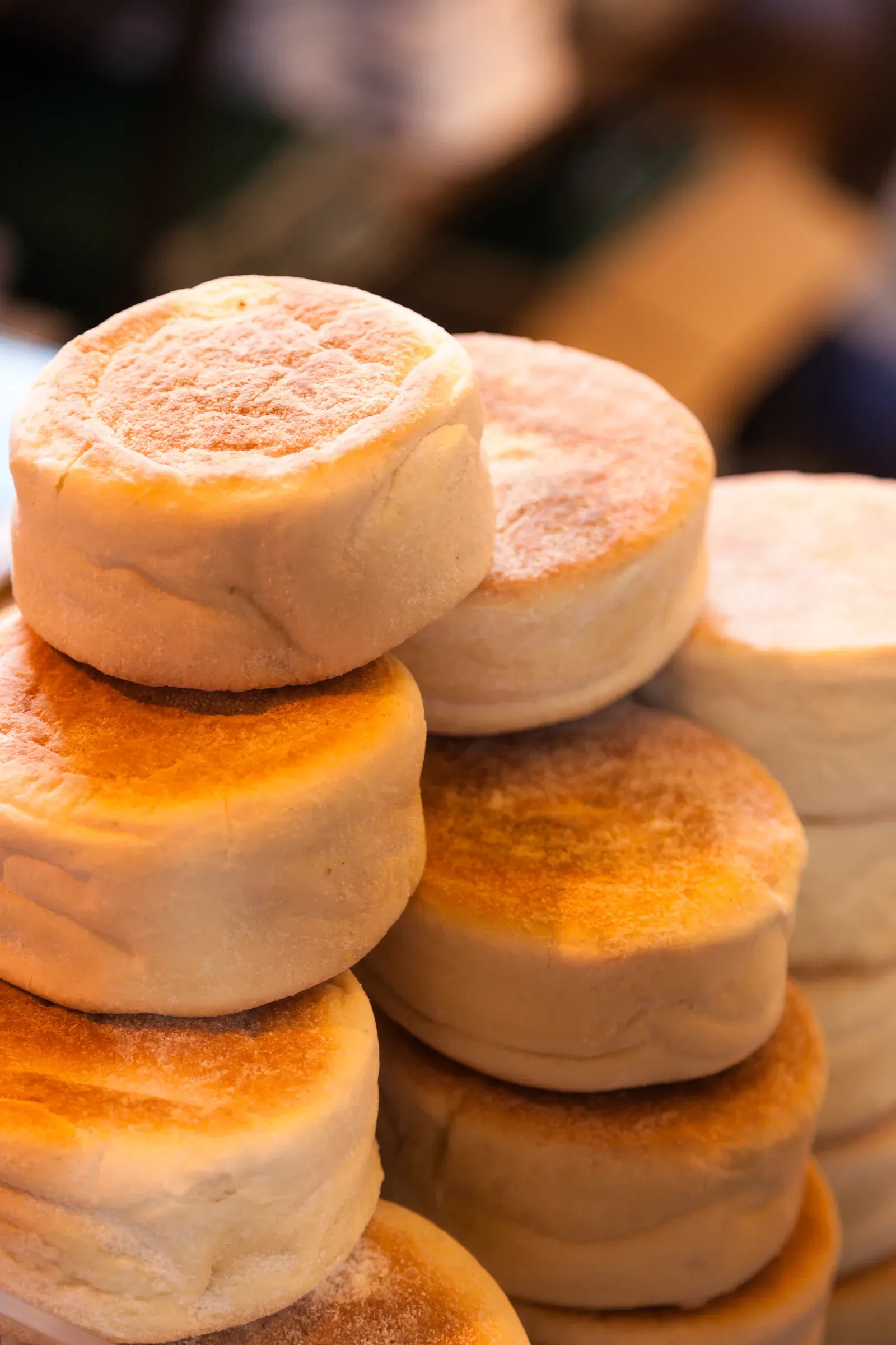 A tall stack of pale, floury English muffins on a market counter