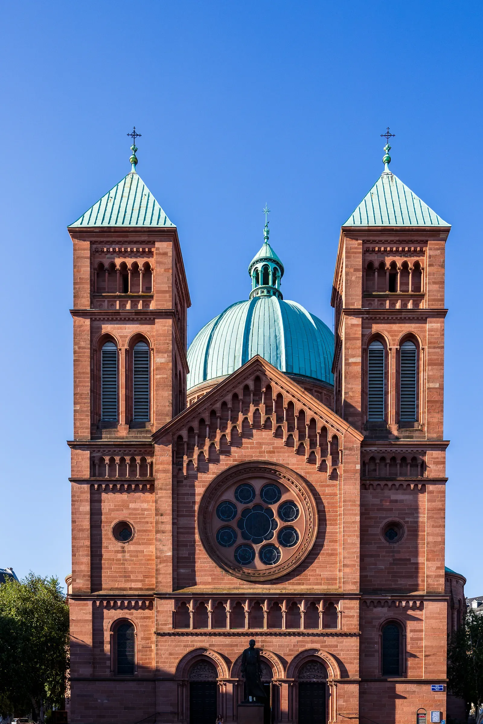 A red sandstone church facade with twin towers and a copper dome, against a clear sky.