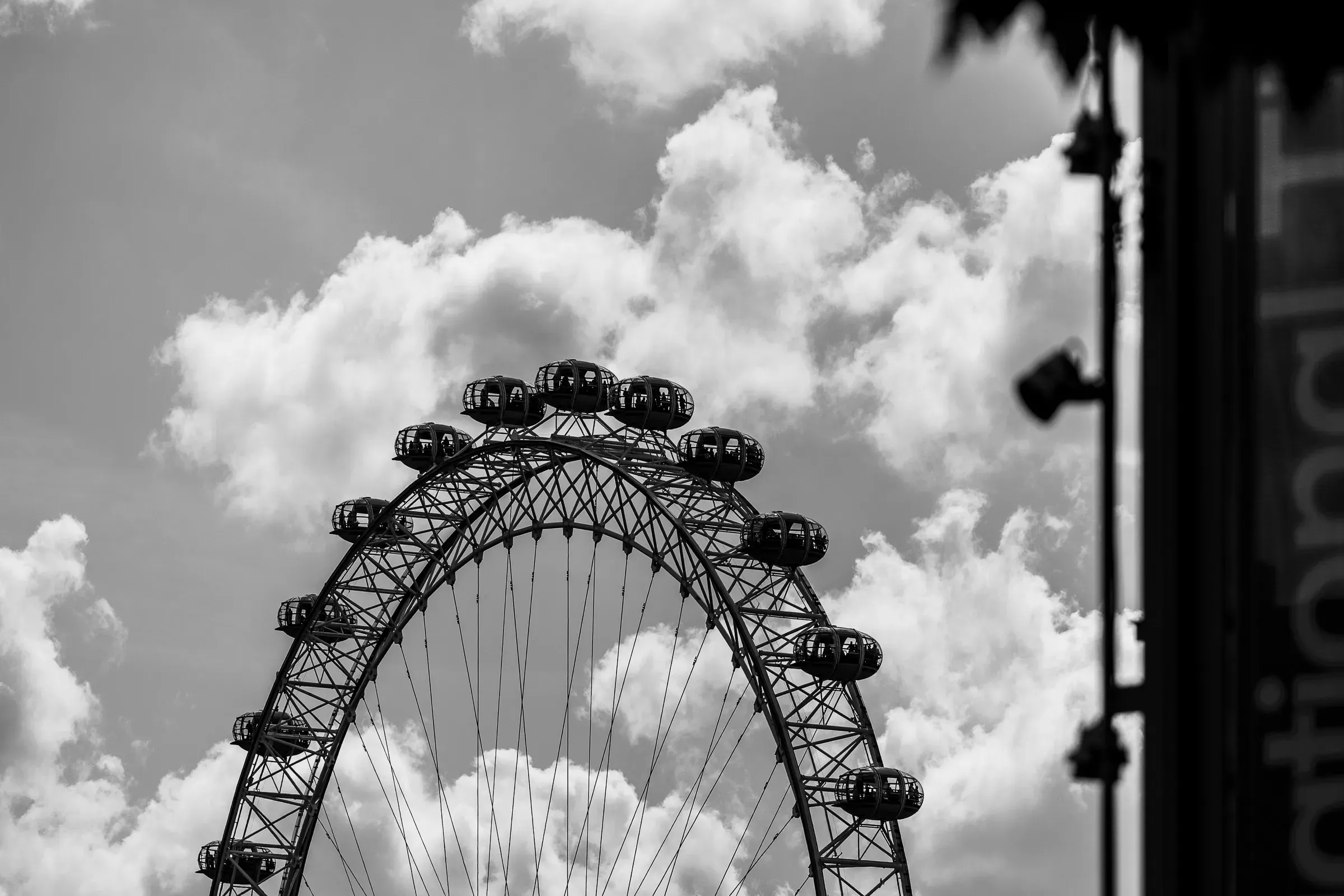 The upper arc of the London Eye against clouds, passenger capsules along the rim, black and white