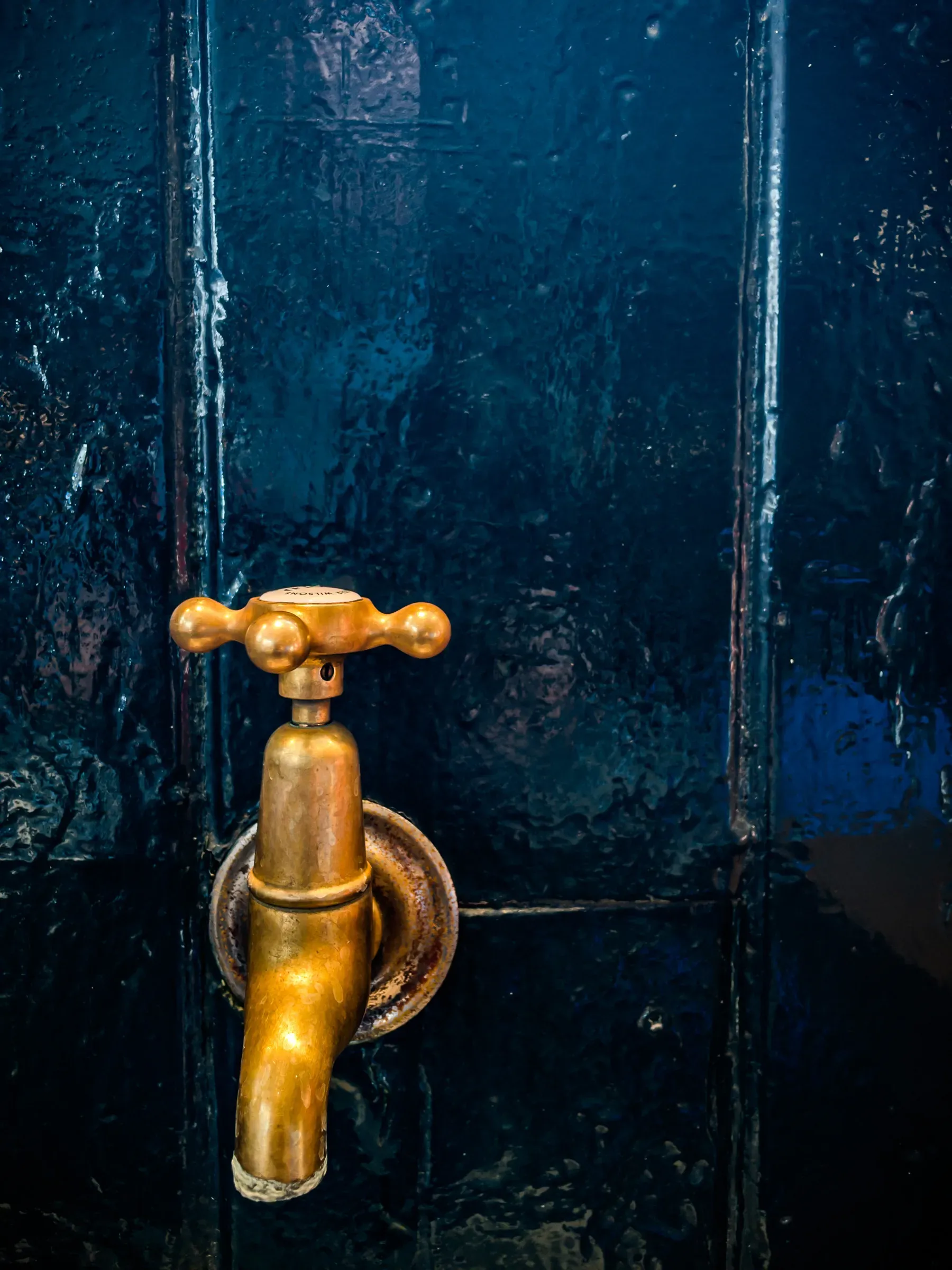 An old brass tap against a glossy dark blue painted door