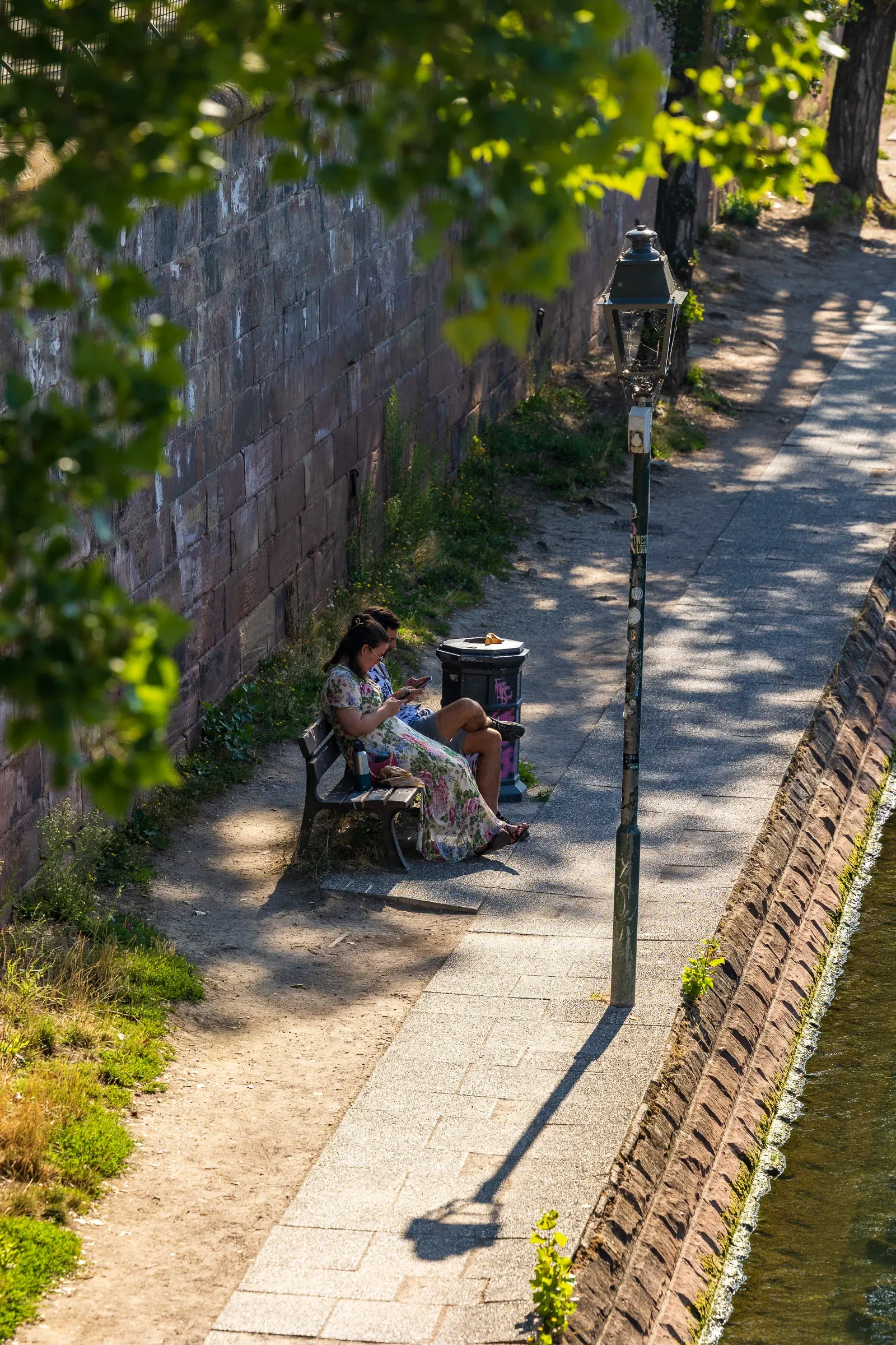 A woman reading on a canal-side bench in dappled shade.