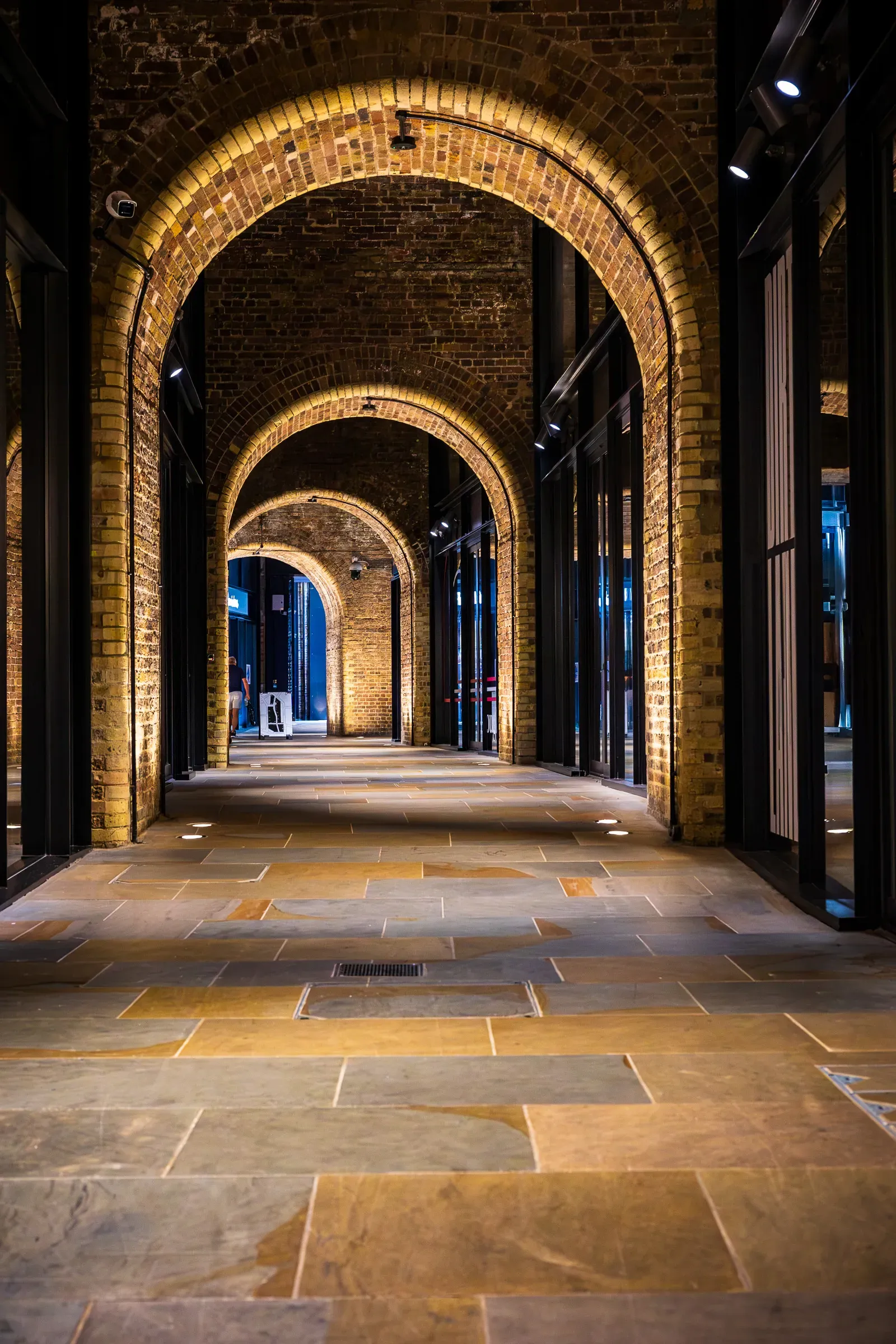 A row of brick archways over a stone-paved passage, shopfronts lit warm on either side