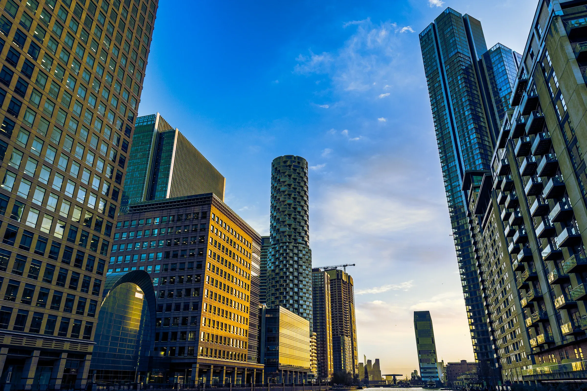 Canary Wharf skyline at dusk — office towers and a distinctive cylindrical residential building catching the last light against a deep blue sky