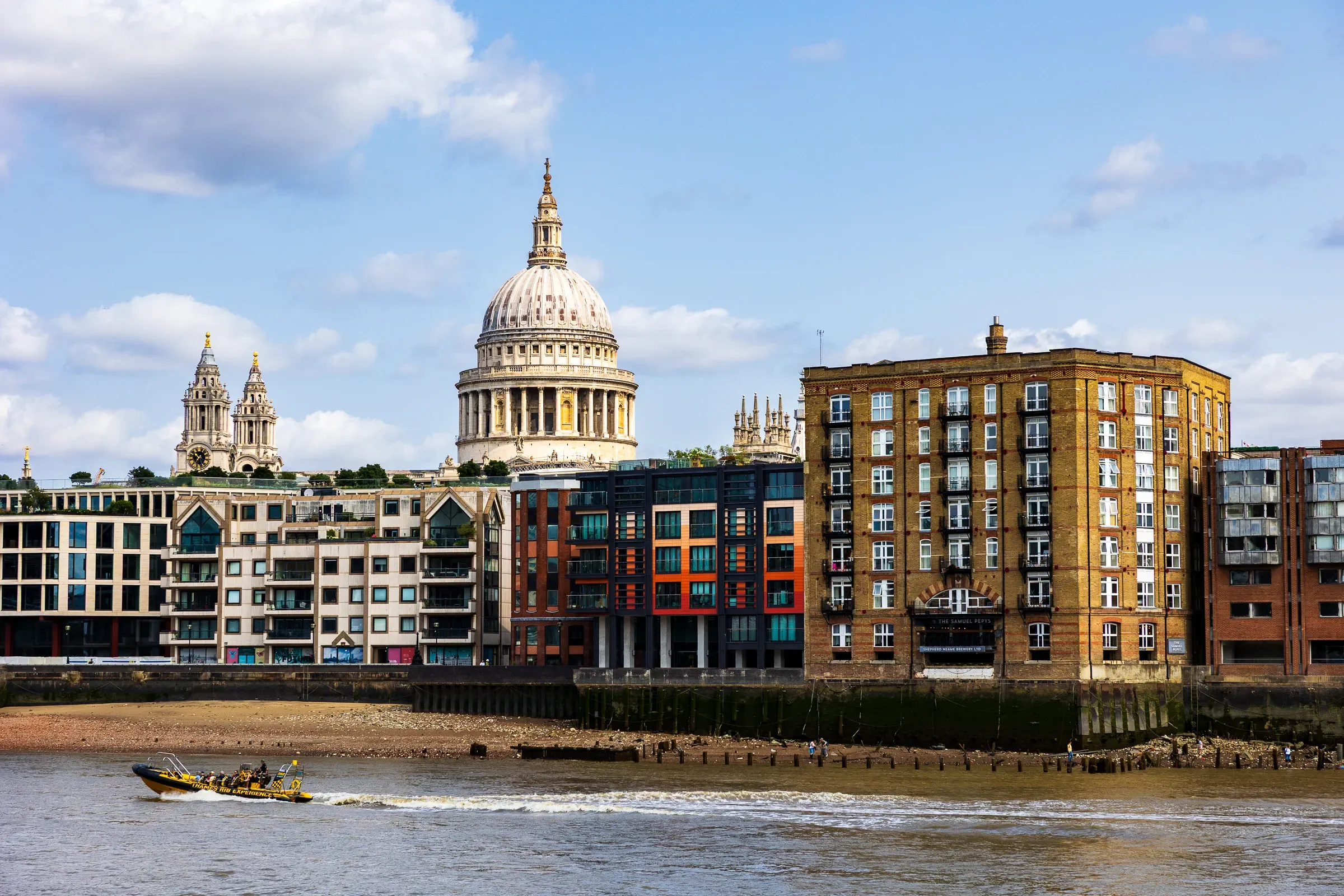 St Paul's Cathedral dome across the Thames, the Millennium Bridge in the foreground, a Thames RIB boat passing at low tide