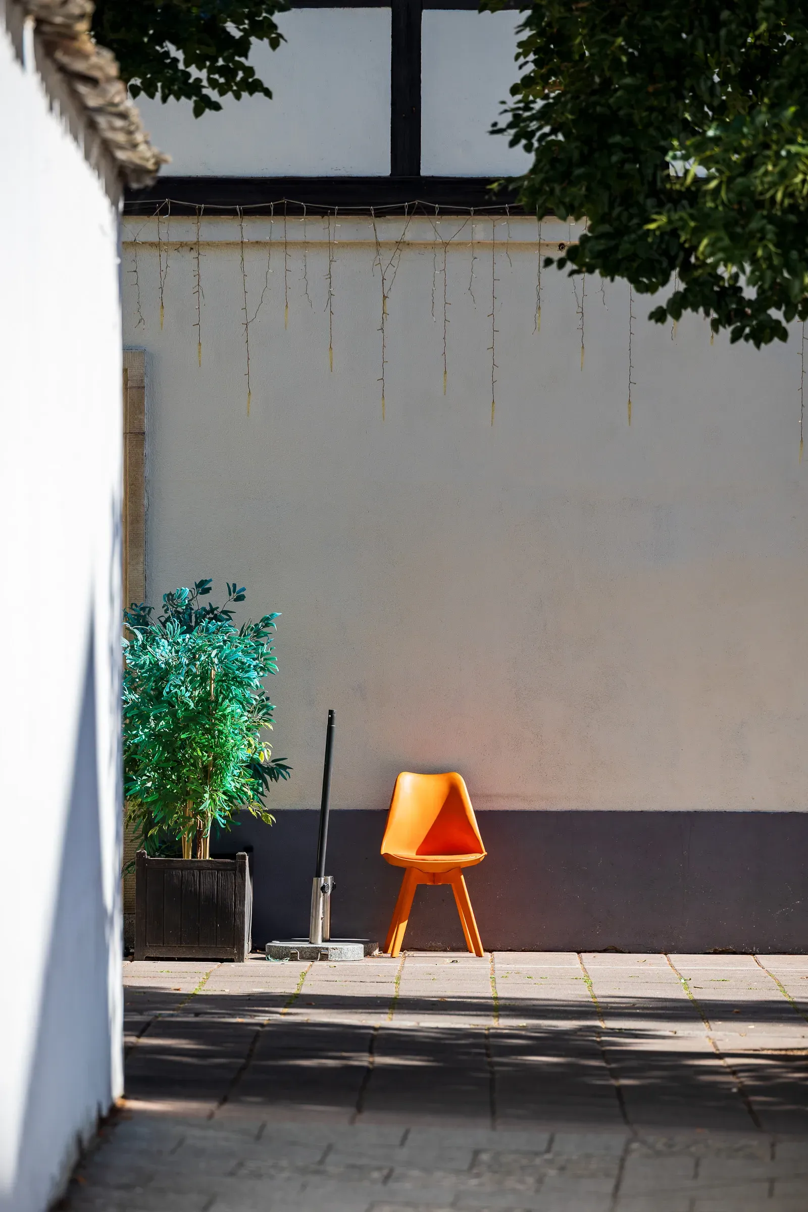 An empty orange chair lit by a shaft of sun against a white courtyard wall.