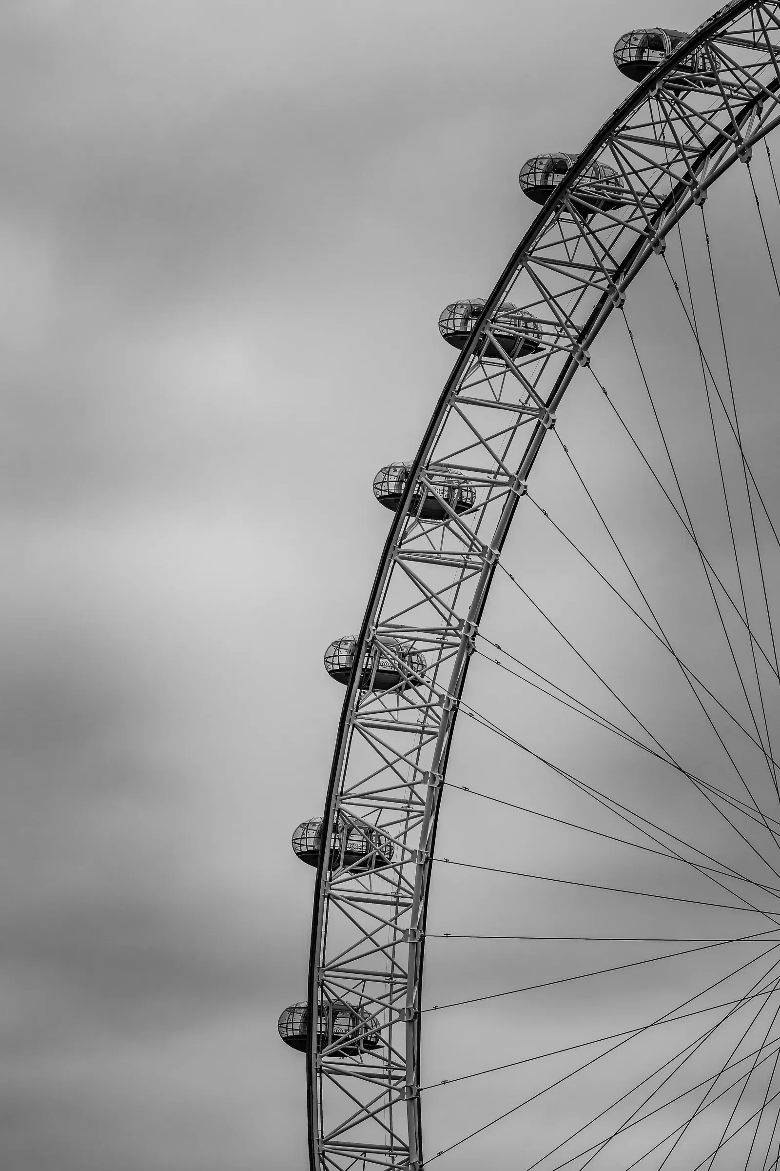 Close view of the London Eye's structure and passenger capsules against an overcast sky, black and white