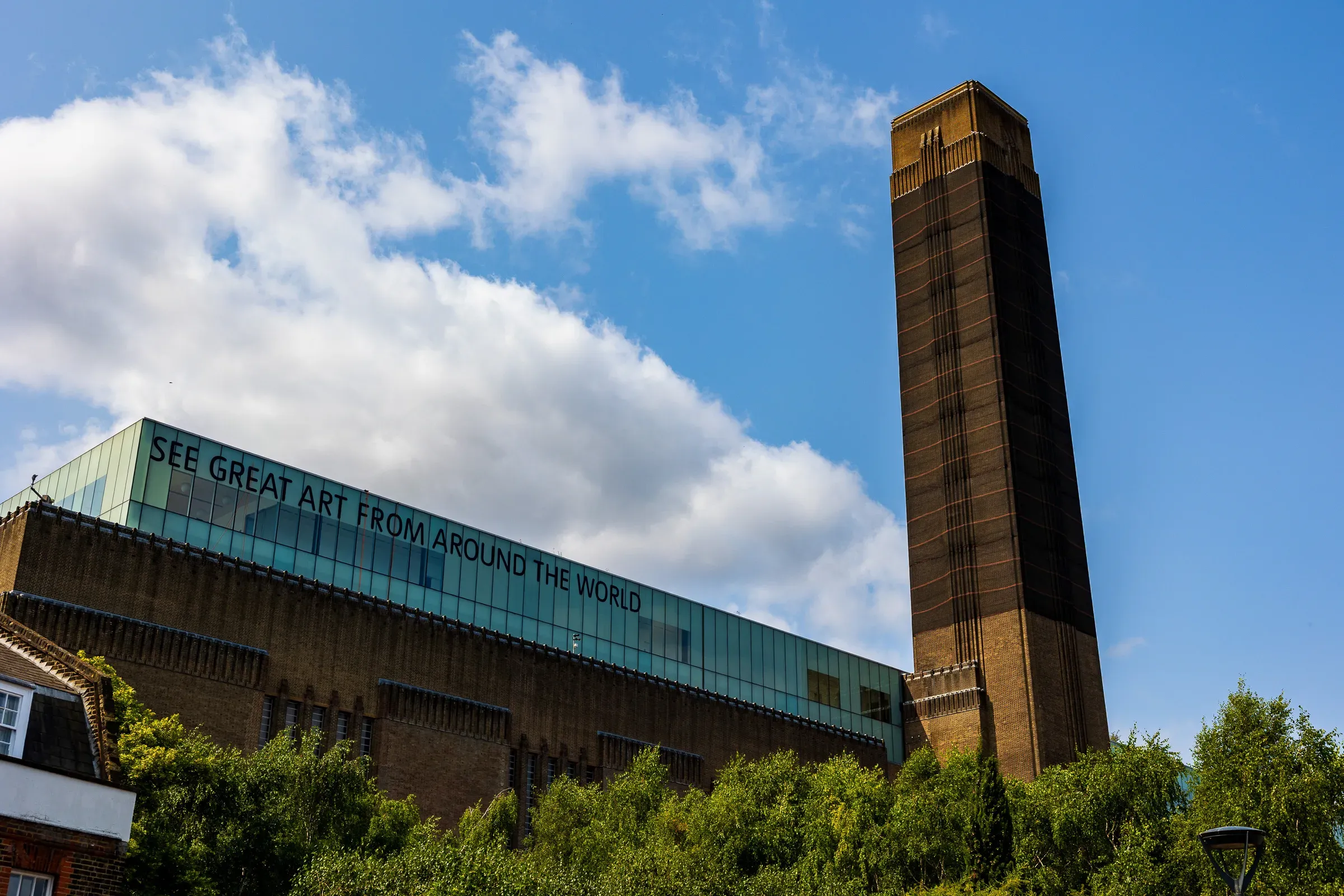Tate Modern's brick chimney and glass extension reading 'See great art from around the world' against a blue sky