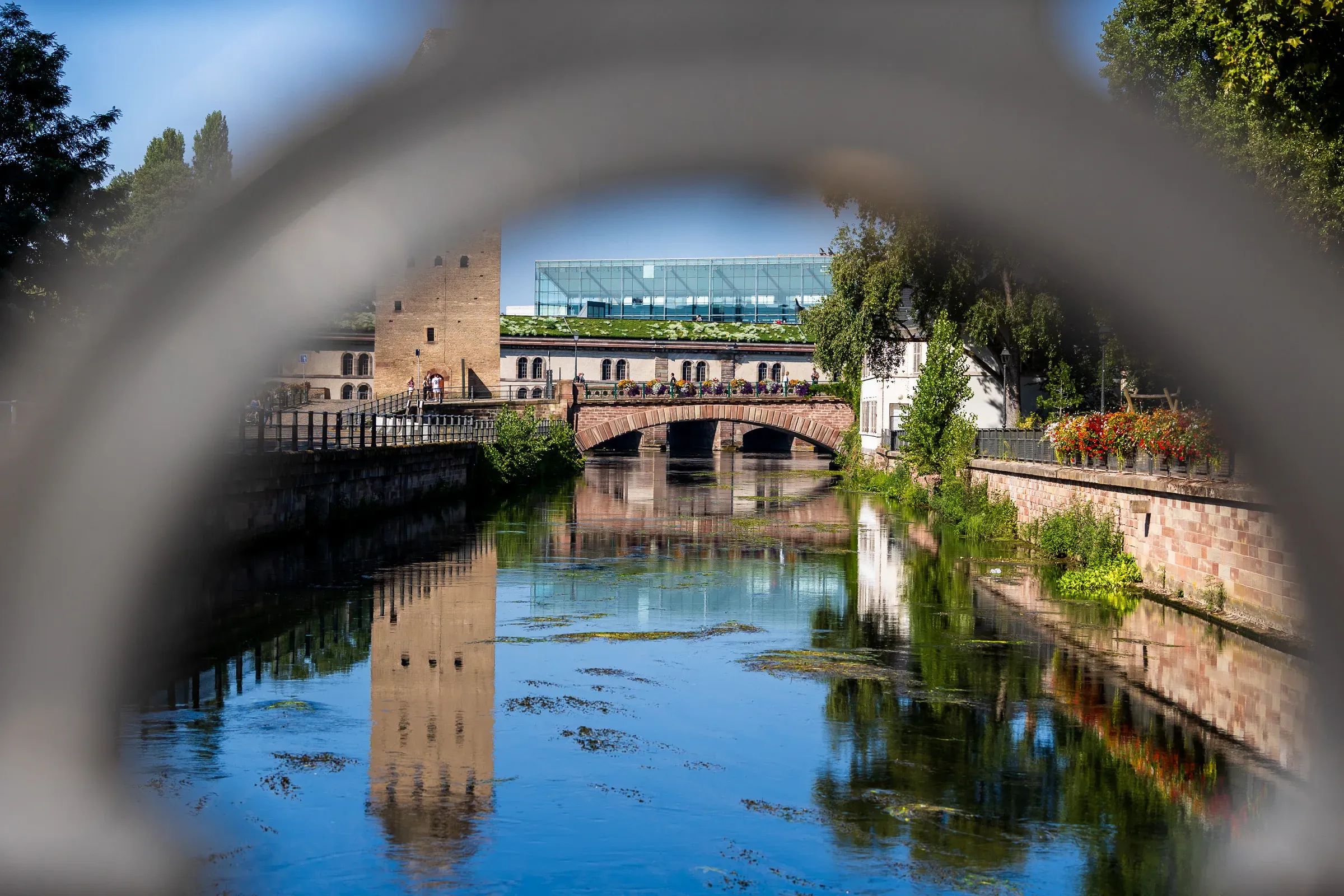 The Ponts Couverts bridge and tower reflected in the Ill, framed through a round iron ring.