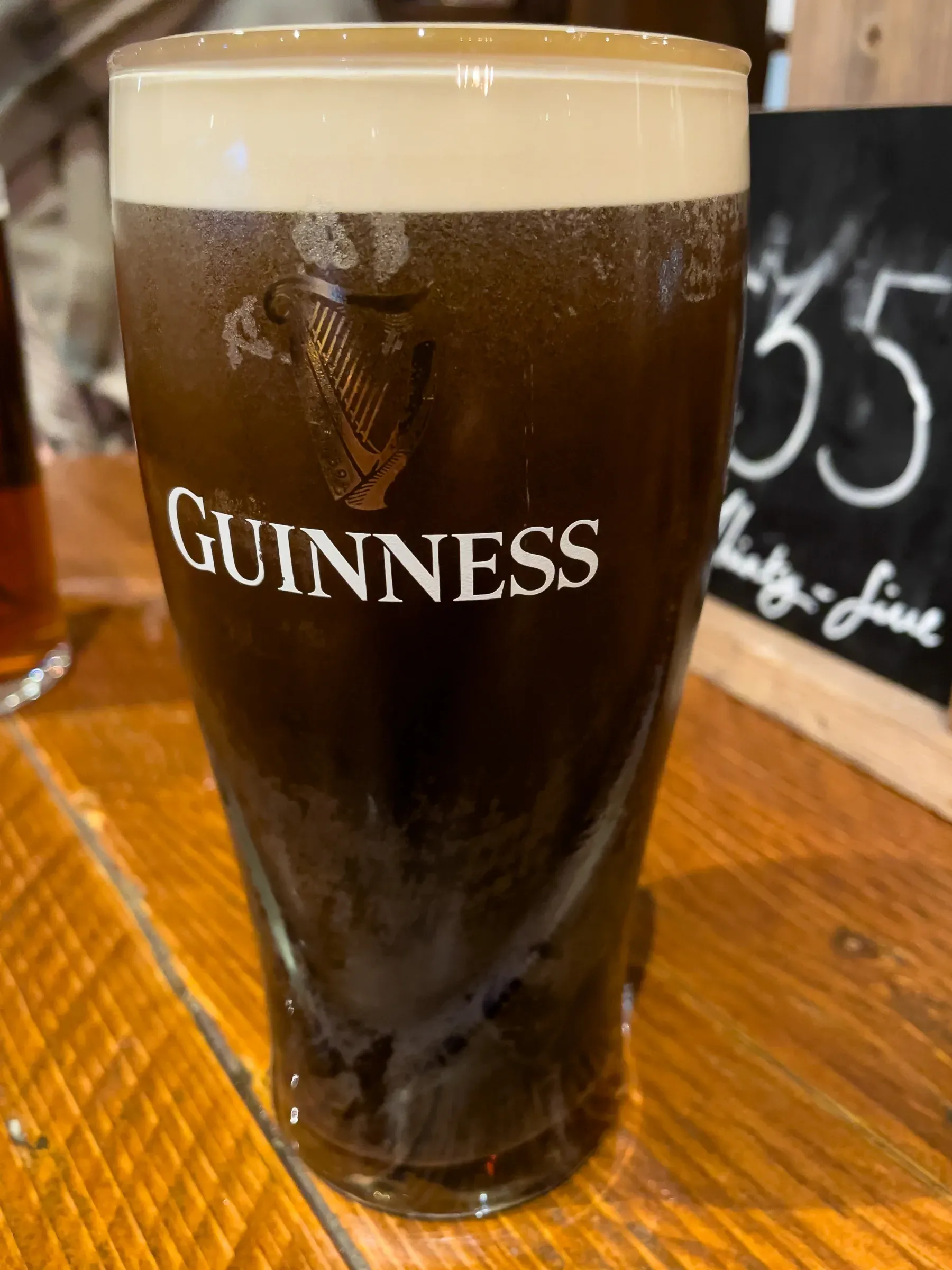 A pint of Guinness on a wooden pub table, cream head settling, a chalked 35 sign blurred in the background
