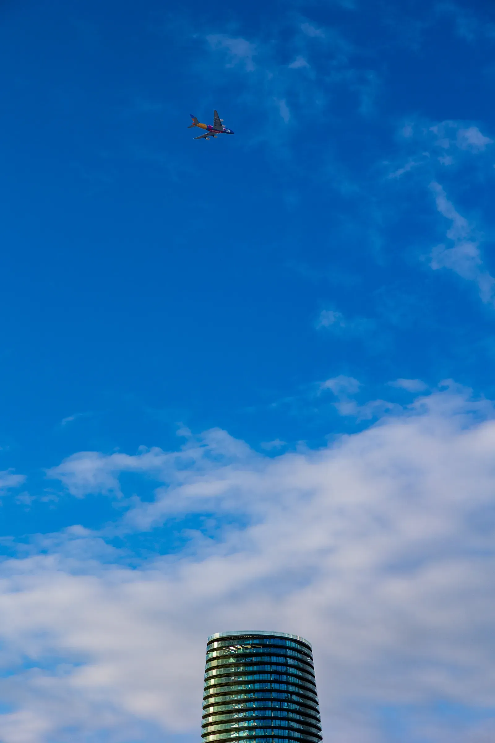 A plane crossing a blue sky above the curved top of a glass residential tower