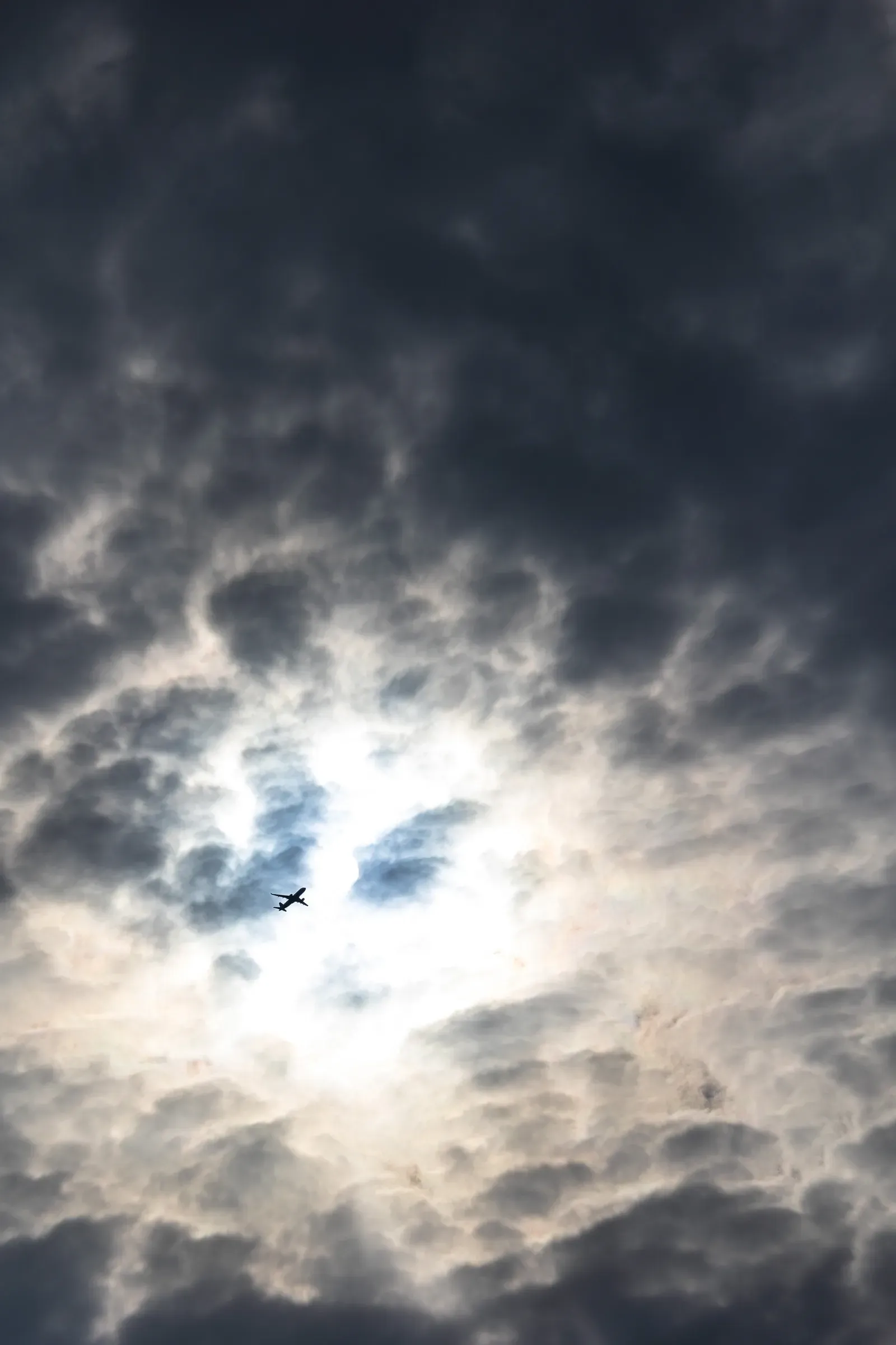 A plane silhouetted in a gap of light between dark storm clouds
