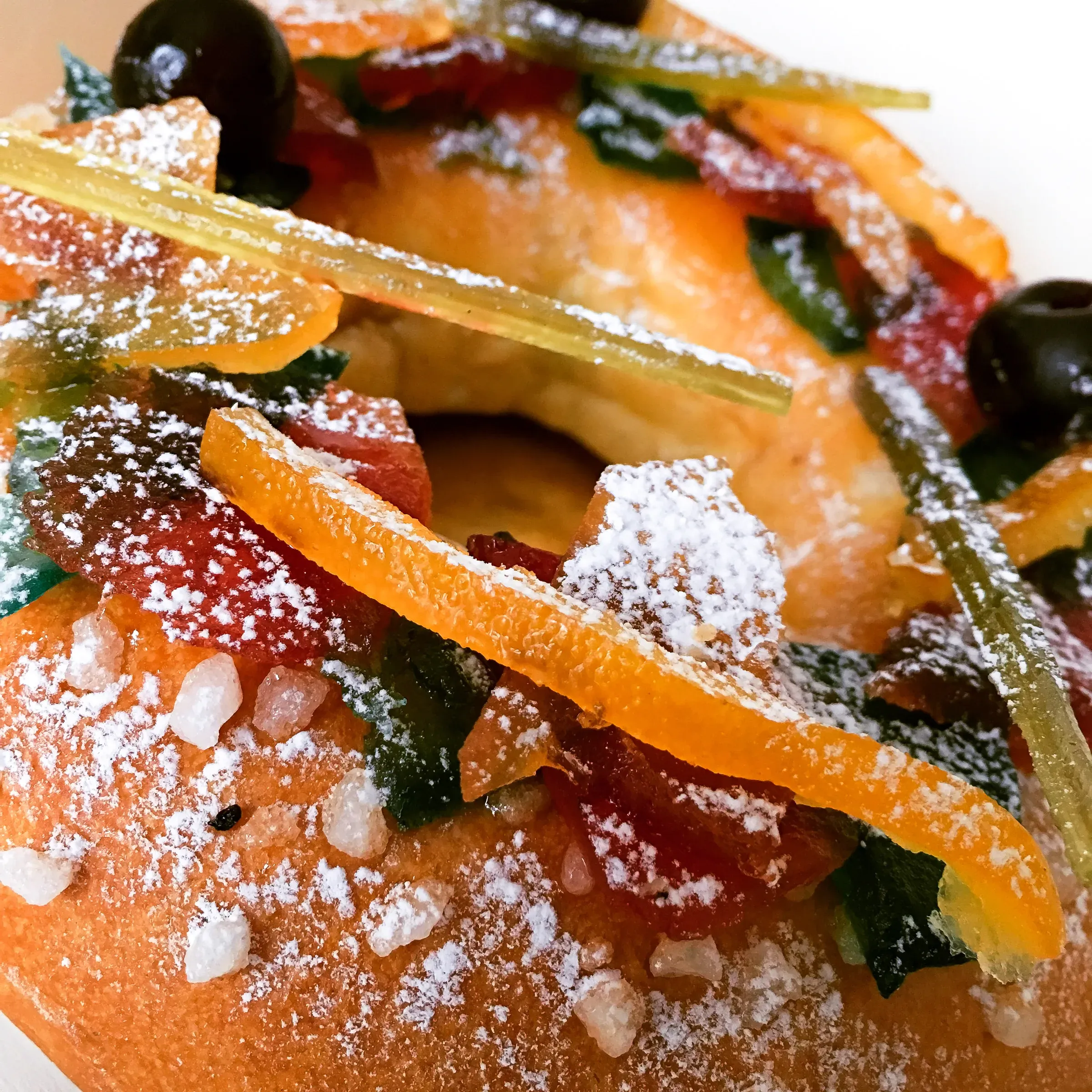 Brioche des rois close-up — candied citrus peel in orange, green and red studded across the glazed brioche ring, powdered sugar dusted