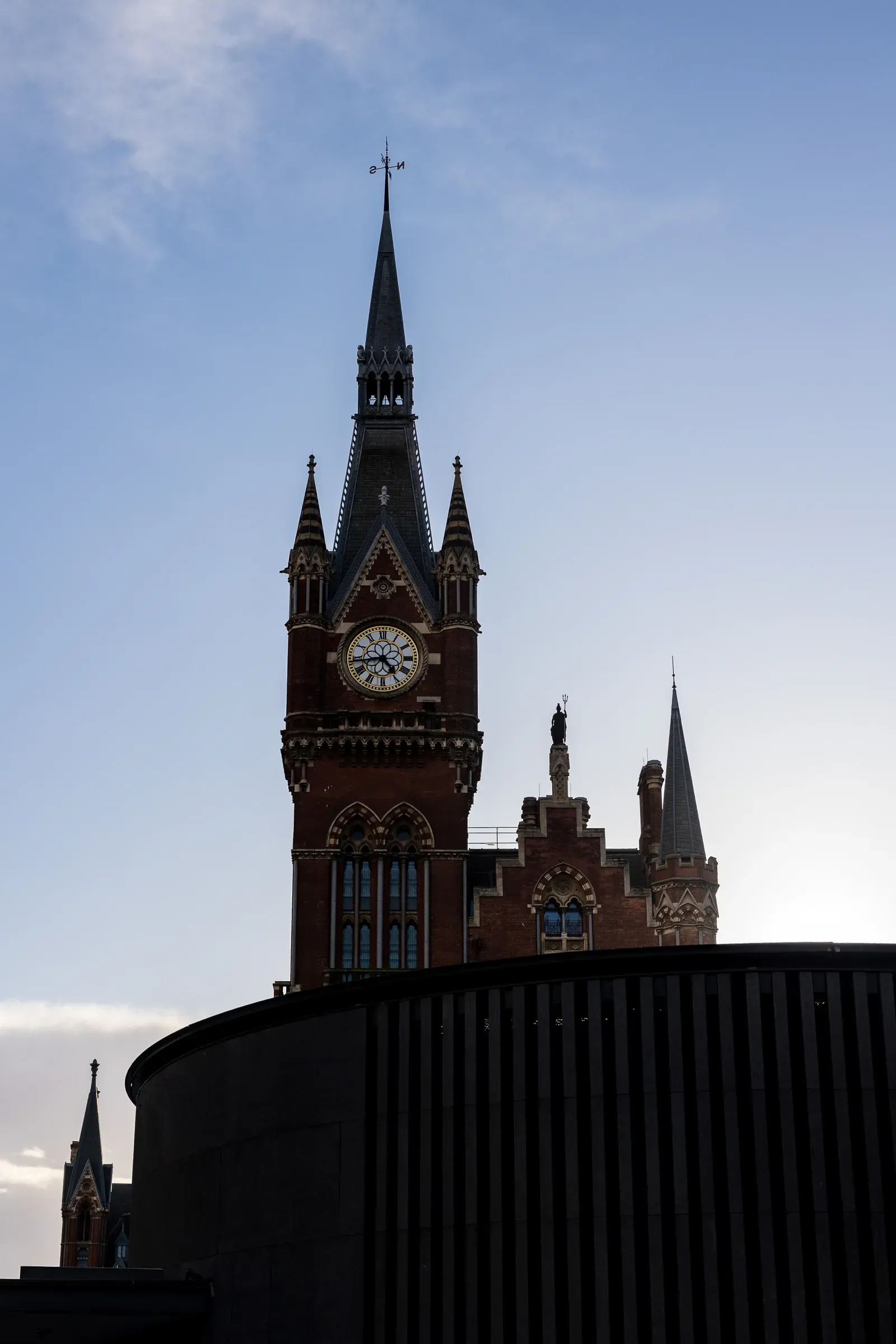 St Pancras's Gothic clock tower and spire against a blue sky, a curved glass roof below